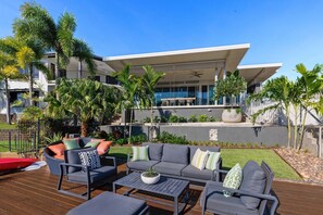 Un espacio exterior moderno con mobiliario, como sofás, una mesa de centro y un comedor, frente a un edificio de estilo contemporáneo.