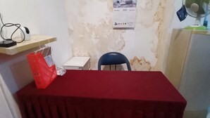 Ein Zimmer mit einem roten Tisch, einem blauen Stuhl, einem Kalender an der Wand, einem Regal mit Telefon und Kabeln sowie einem Kühlschrank.