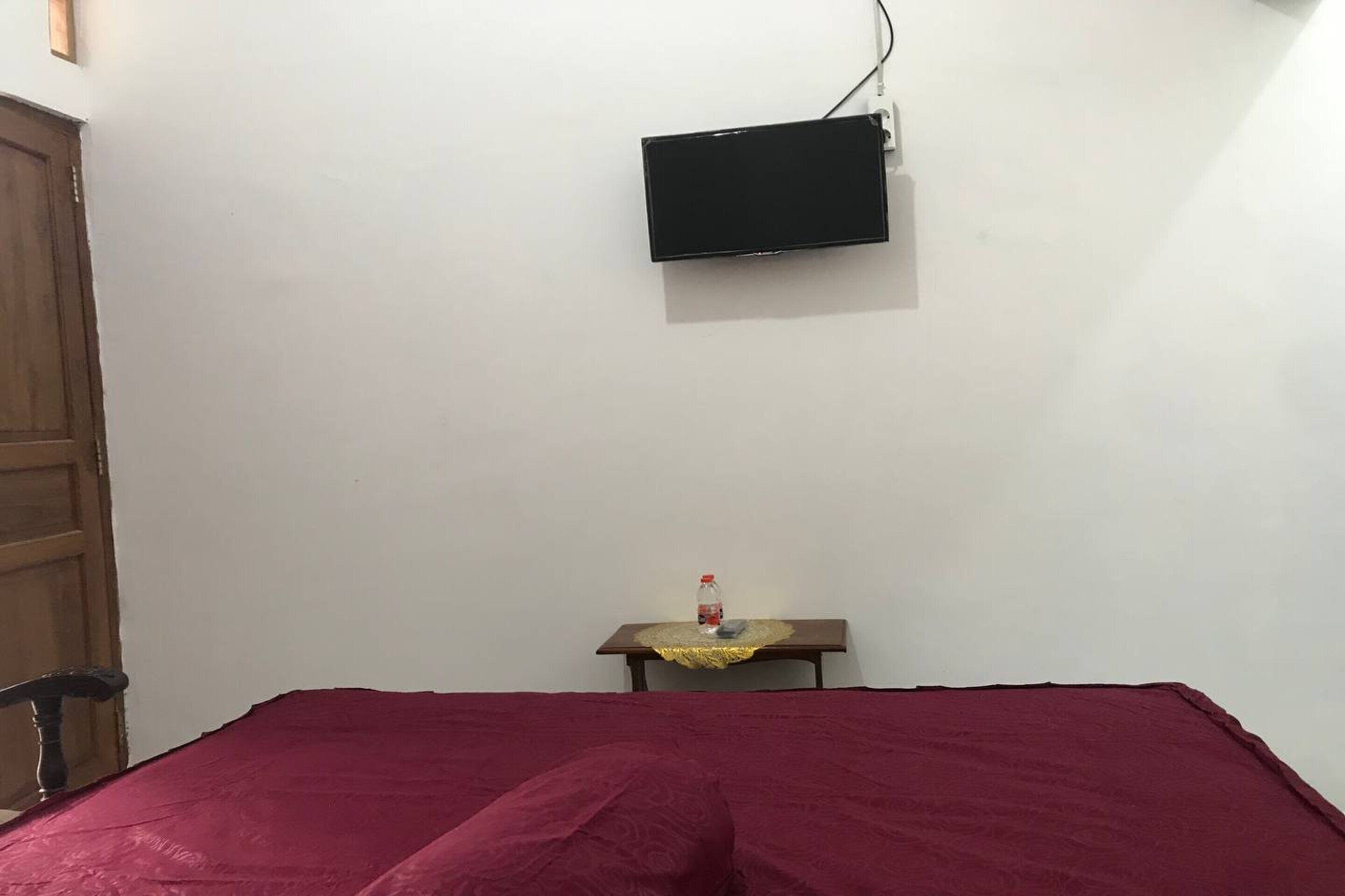 A room with a bed, a television mounted on the wall, and a small table with a bottle on it.