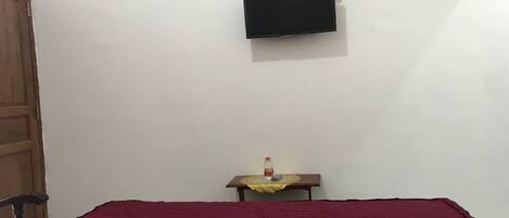 A room with a bed, a television mounted on the wall, and a small table with a bottle on it.