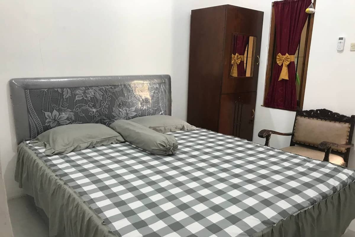 Ein Bett mit karierter Bettdecke, ein Kopfteil mit Blumenmuster und ein Kleiderschrank mit Spiegel und Vorhängen.