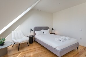 A modern bedroom with a large bed, a white chair, two bedside tables, and a skylight. - GuestReady - Urban retreat in Boavista (Boavista)