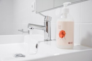 A bathroom with a modern faucet, a bottle of soap, and a clear glass shower area. - GuestReady - Urban retreat in Boavista (Boavista)