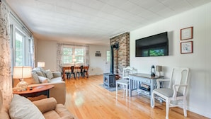Un salón amplio con chimenea, suelo de madera, una zona de comedor con sillas y un televisor montado en la pared.
