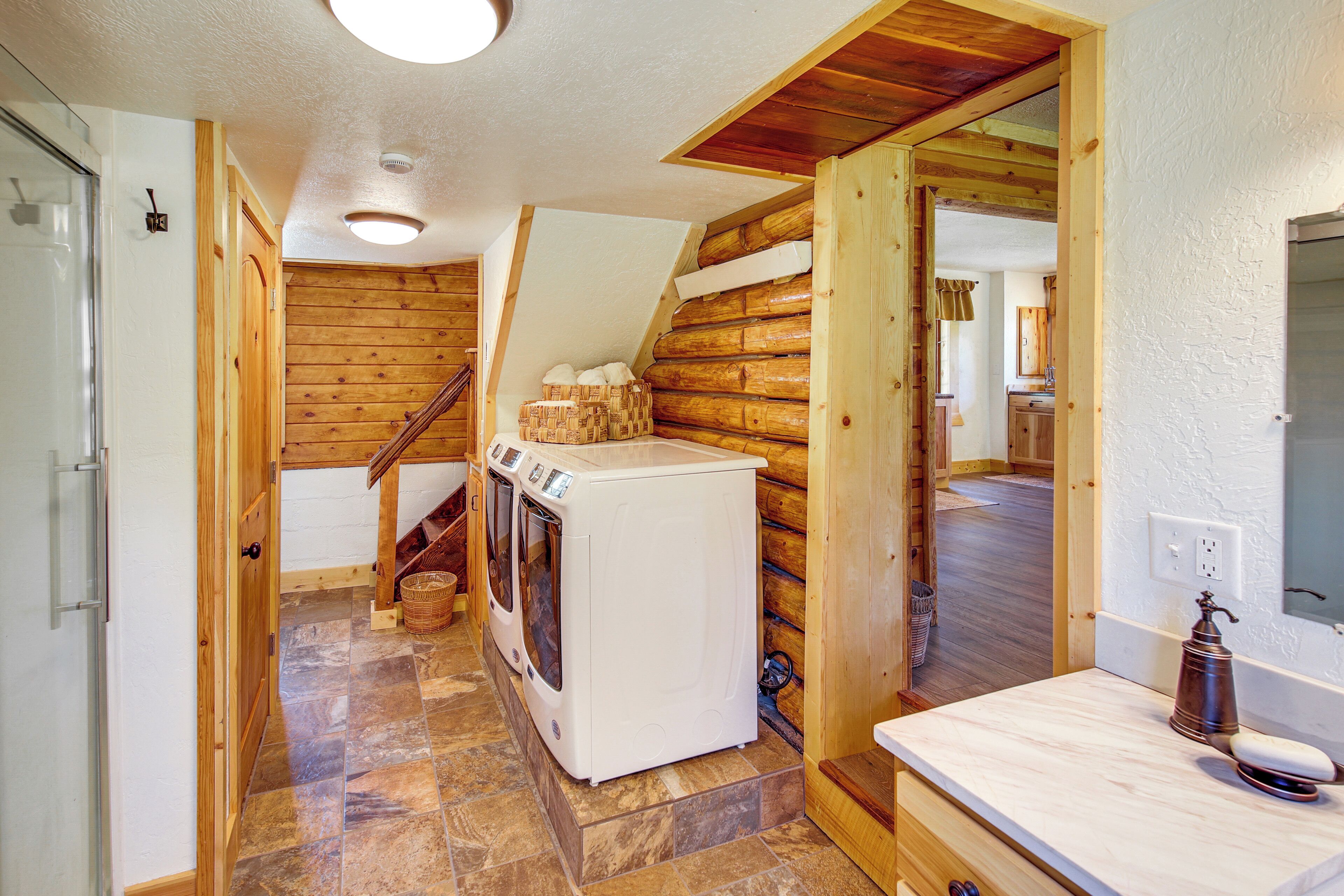 A laundry room with a washing machine and dryer, wooden walls, and a stone-tiled floor.