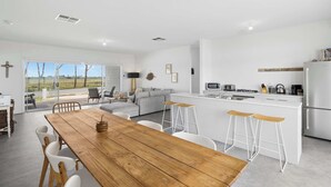 A modern kitchen with white cabinetry, a dining area with a wooden table and white chairs, and a bar area with stools.