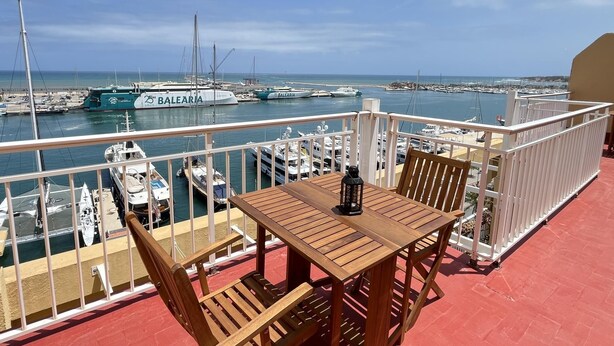 Un balcón con mesa y sillas de madera, con vista a un puerto deportivo lleno de barcos y yates.