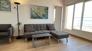 Una sala moderna con un sofá seccional, una mesita y una lámpara de pie. Se ve una ventana grande que ofrece vistas de la ciudad.