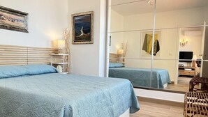 Un dormitorio moderno con una cama grande, un espejo, un televisor y una pequeña zona de estar.