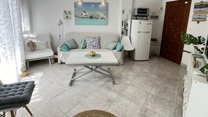 A modern living room with a white sofa, a dining table, and a kitchen area. - Flat El Retiro 4 people with swimming pool. (Dénia)