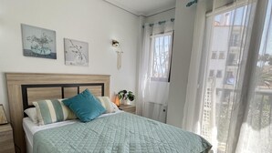A bedroom with a bed, a nightstand, a wall-mounted light, and a window with curtains. - Flat El Retiro 4 people with swimming pool. (Dénia)