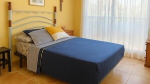 A bedroom with a bed, a nightstand, a chair, a picture on the wall, and a window with curtains. - 2-bedroom flat in Playasol II (Dénia)