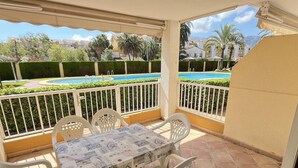 A covered outdoor patio with a table and chairs, a pool in the background, and a view of the surrounding area. - 2-bedroom flat in Playasol II (Dénia)