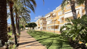 A pathway lined with palm trees leading to a yellow building with balconies. - 2-bedroom flat in Playasol II (Dénia)