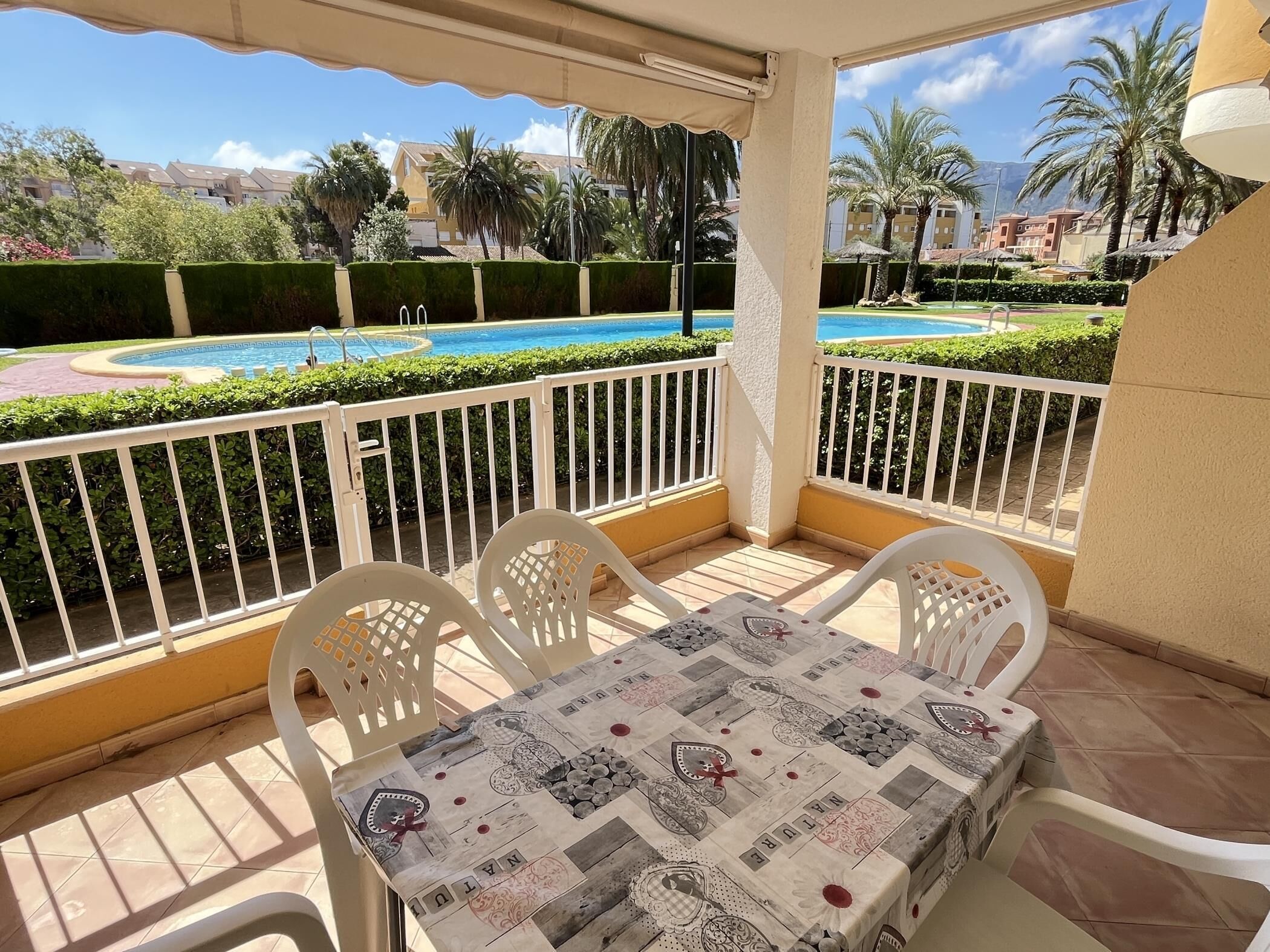 Ein Balkon mit Tisch und Stühlen, mit Blick auf einen Swimmingpool und einen angelegten Garten.