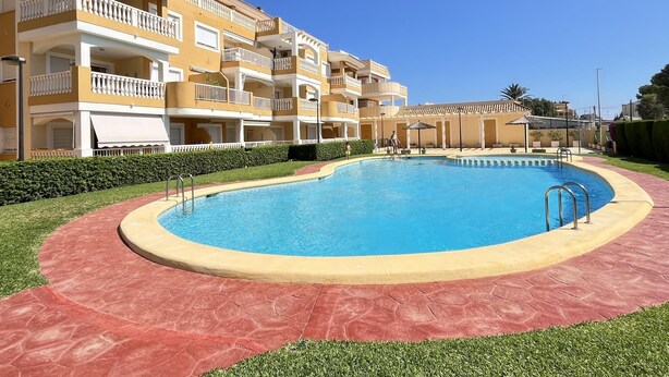 A swimming pool surrounded by a red tiled walkway, with a multi-story building featuring balconies in the background. - 2-bedroom flat in Playasol II (Dénia)