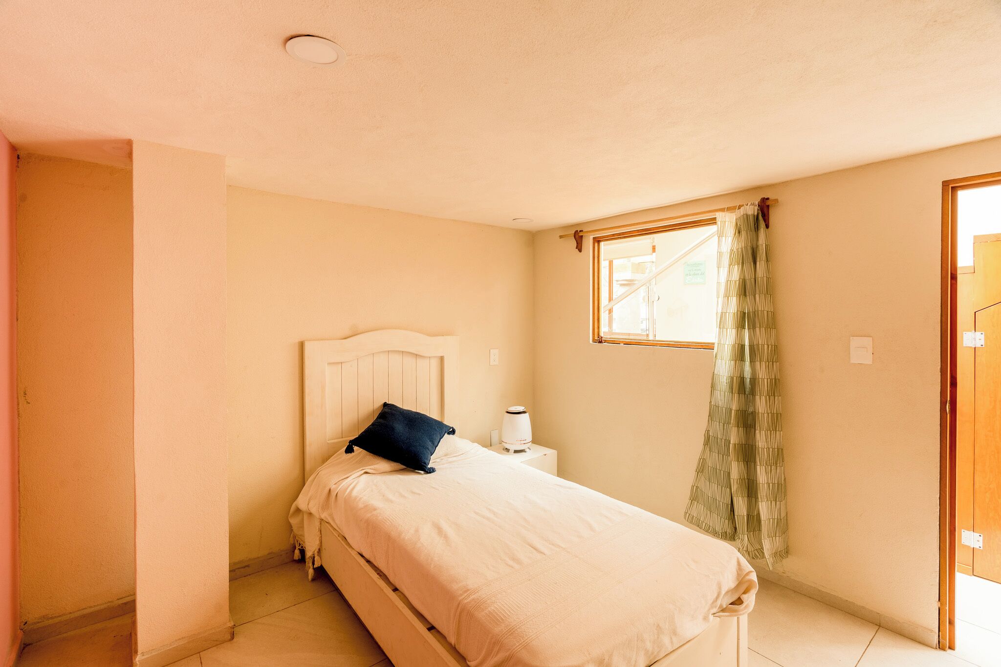 A bedroom with a bed, a nightstand, a window with curtains, and a door.