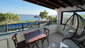 A balcony with a table and chairs, a hanging chair, and a view of the sea and greenery. - Alp Ateş Suit  (Ayvacik)
