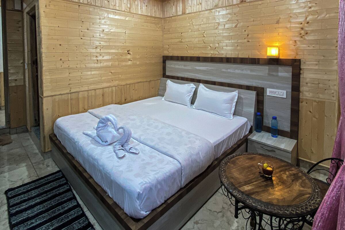 Un dormitorio con paneles de madera, una cama, una mesita de noche y una pequeña mesa redonda con una lámpara.