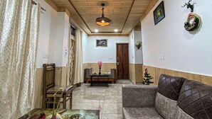 Ένα σαλόνι με ξύλινη οροφή, έναν καναπέ, ένα τραπεζάκι σαλονιού με διακοσμητικά αντικείμενα και ένα μικρό χριστουγεννιάτικο δέντρο.