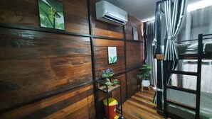 Een kamer met houten lambrisering, een metalen plank met planten, een rode prullenbak en een raam met gordijnen.