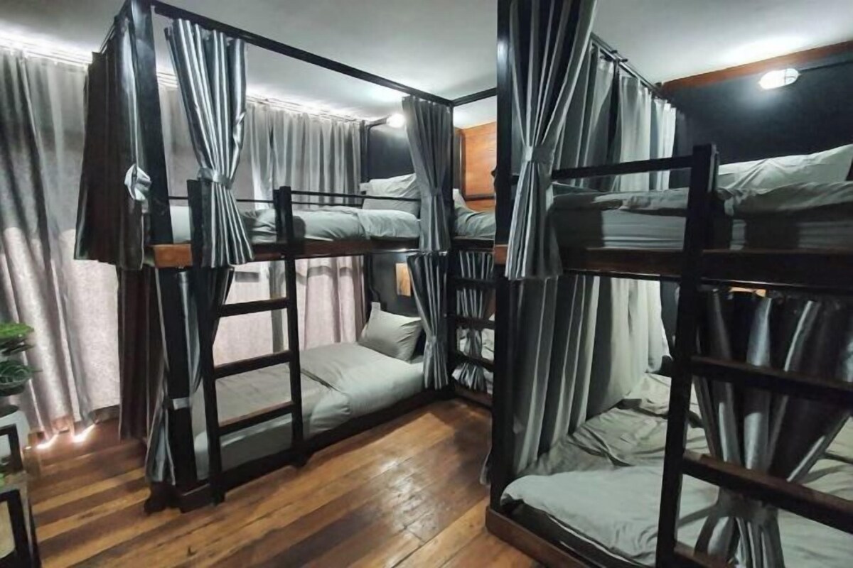 A room with bunk beds, wooden flooring, and curtains.