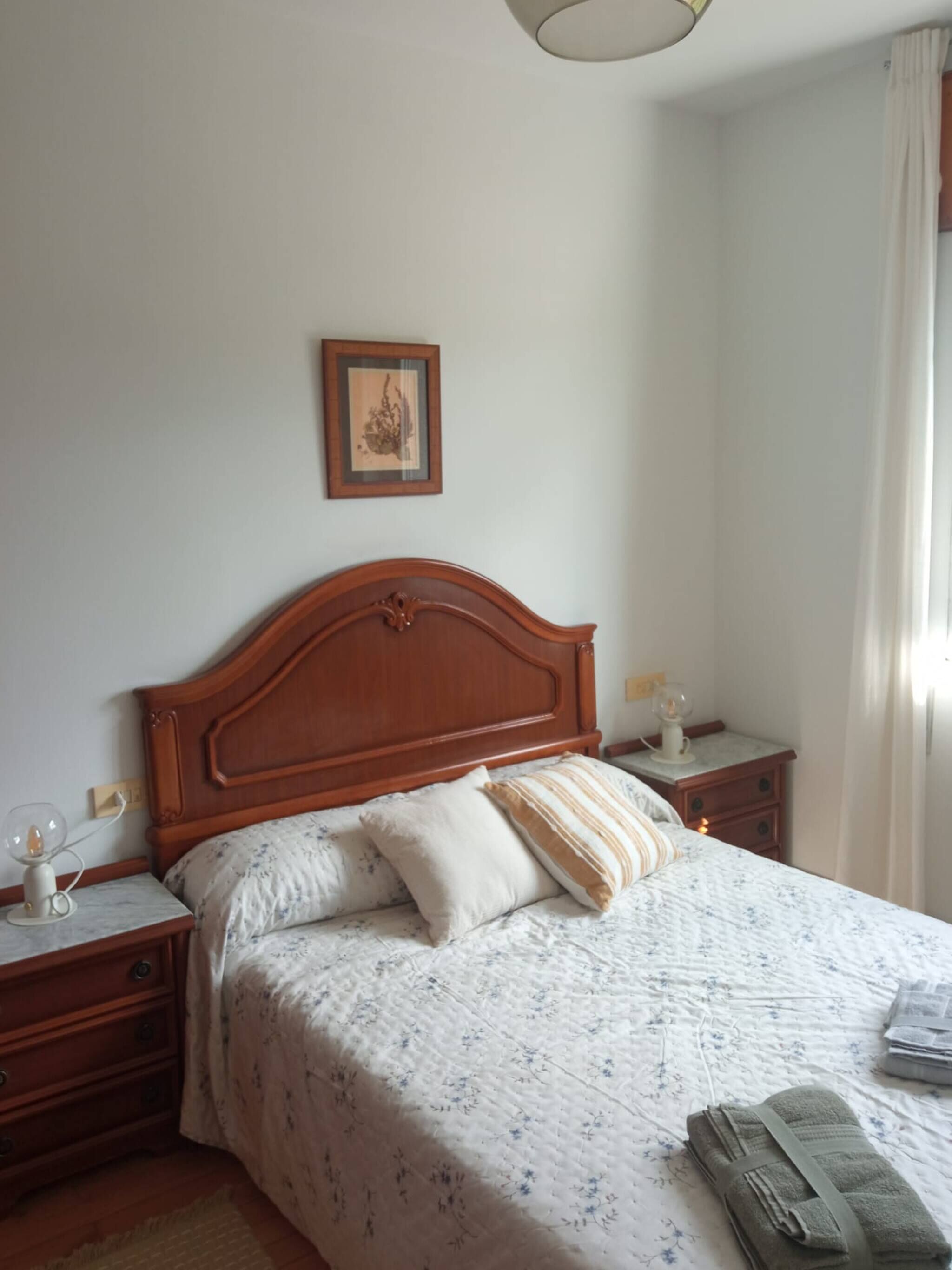 Een keurig opgemaakt bed met een bloemenbedekker, een houten hoofdbord en een nachtkastje met een lamp.