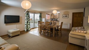 A living room with a TV, a dining area with wooden chairs, a sofa, and a kitchen in the background. - Drws Nesa - sleeps 6 guests  in 3 bedrooms (Pwllheli)