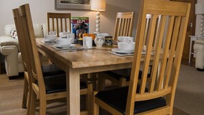 A dining area with a wooden table and chairs, a lamp, and a framed picture on the wall. - Drws Nesa - sleeps 6 guests  in 3 bedrooms (Pwllheli)