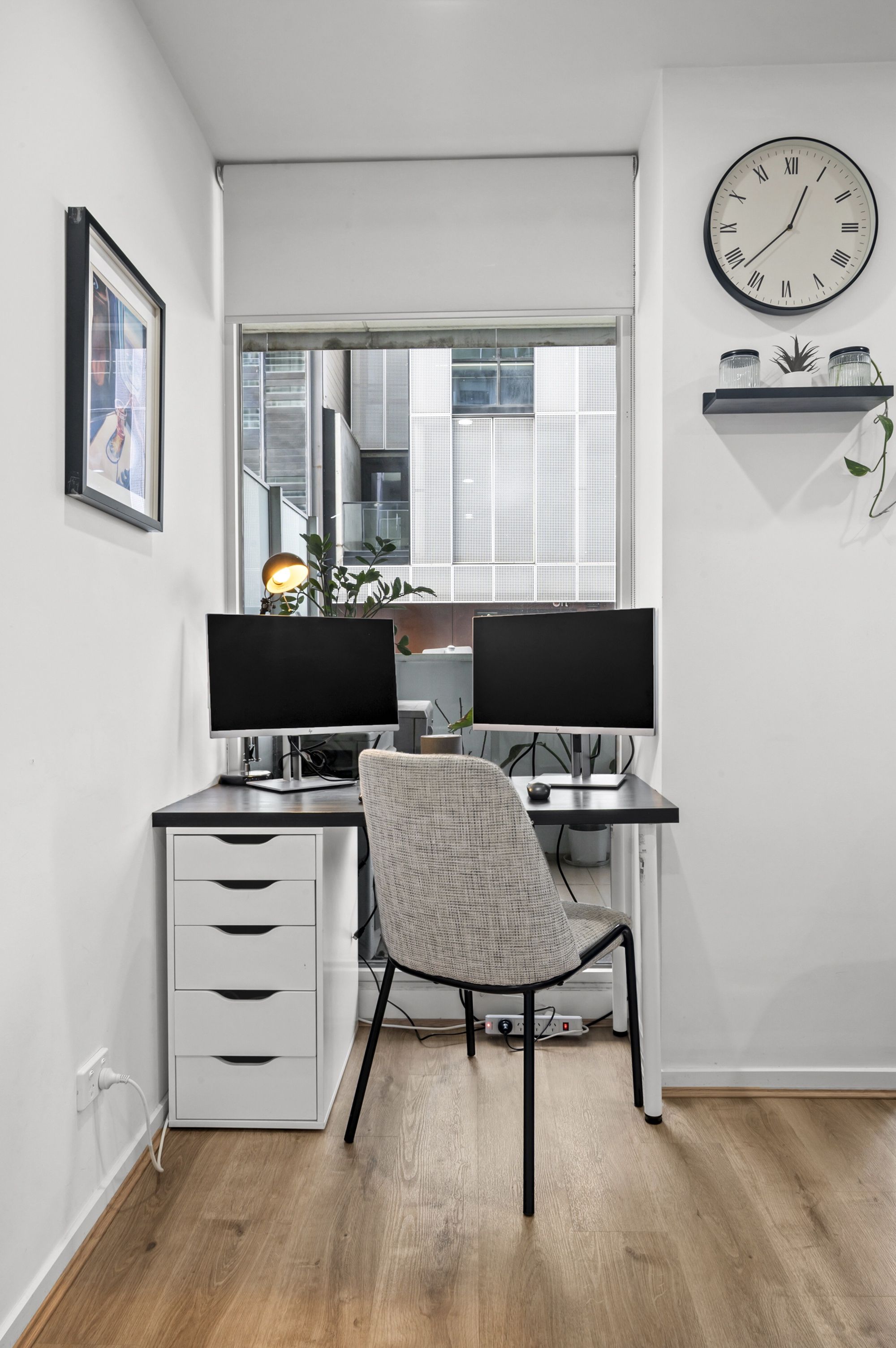 A modern office space with a desk, two monitors, a chair, a clock, and a window with a city view.