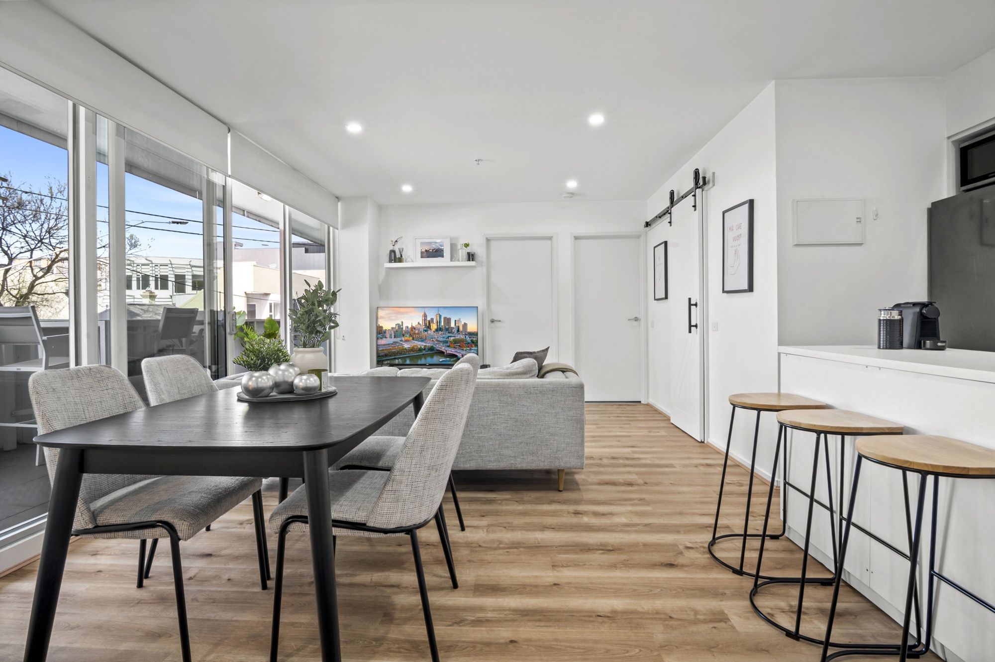 A modern kitchen with a dining area, wooden flooring, and large windows.