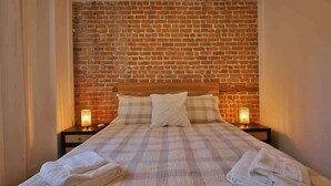 Ein Bett mit einem Holzkopfteil, zwei Nachttischlampen und einer karierten Tagesdecke.