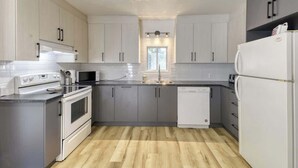 A modern kitchen with grey cabinets, a white refrigerator, a dishwasher, and a microwave. - 5BR Chalet with Hot Tub & Lake Access (Mont-Blanc)