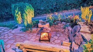 Une terrasse en pierre avec un foyer, un banc en bois et un mur en briques orné de plantes.