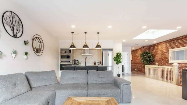 Ein modernes Wohnzimmer mit einem grauen Ecksofa, einem Holztisch und einer Küche im Hintergrund.