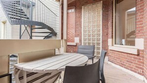 Ein Balkon mit einer Wendeltreppe aus Metall, einem runden Tisch und zwei Stühlen.