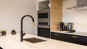 Une cuisine moderne avec un robinet noir, un four encastré et une machine à café posée sur le plan de travail.