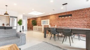 Une cuisine moderne avec un mur en briques, un coin repas avec une table et des chaises, et un canapé gris dans le salon.