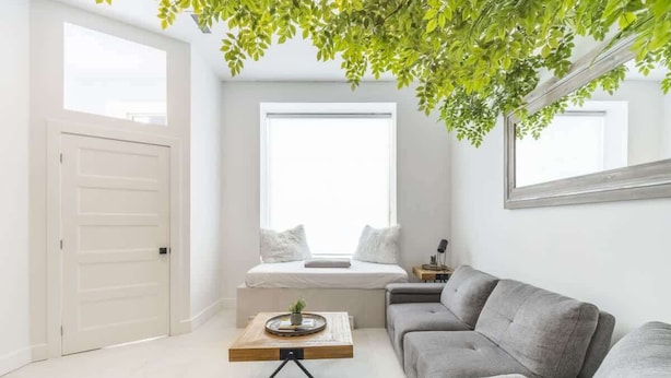 Un salón moderno con un sofá gris, una mesita de centro, una cama con ropa de cama blanca y un ventanal grande.