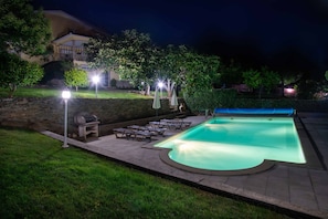 Une piscine bordée de pierres, entourée d’un espace patio aménagé avec des chaises longues et des parasols.