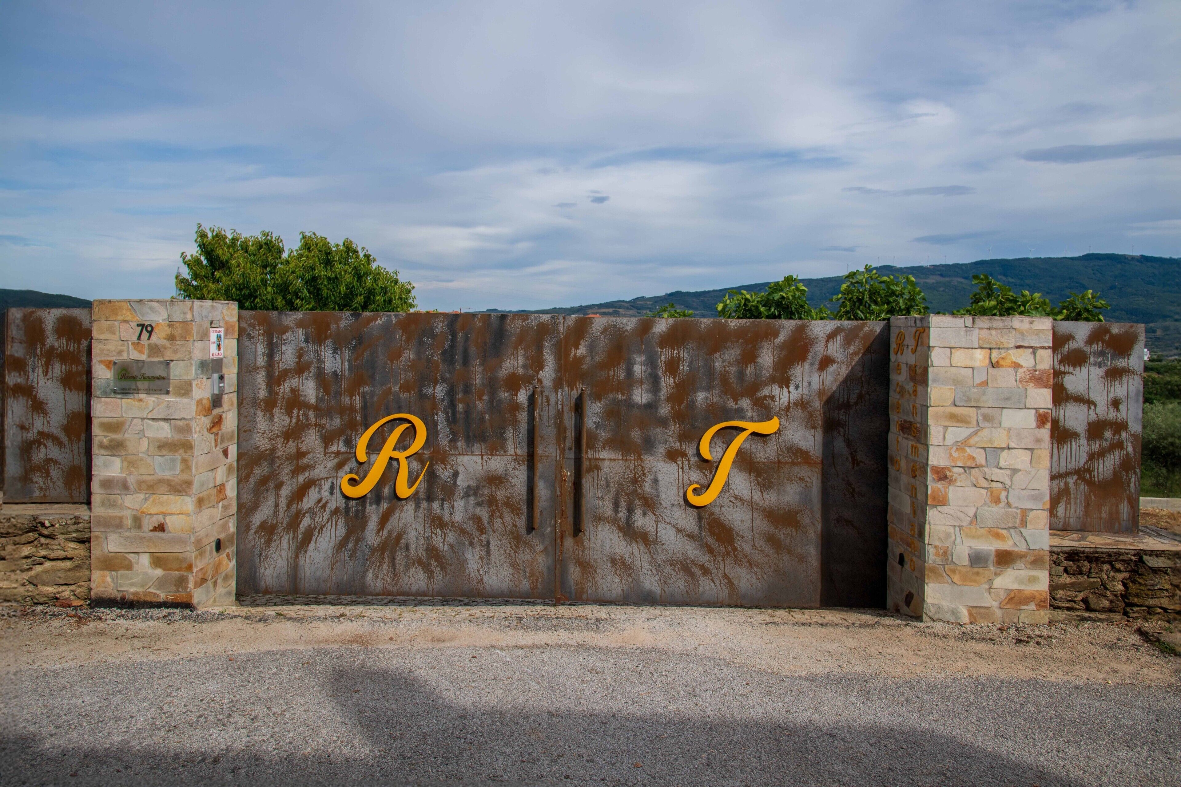 Una reja metálica con las letras 'R' y 'T' en amarillo, ubicada en un paisaje rural con colinas al fondo.