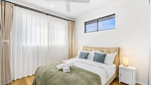 Un lit bien fait, avec une couverture verte et des serviettes blanches, une table de chevet avec une lampe et un ventilateur de plafond.