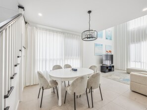 A modern living room with a round dining table, six chairs, a television, and a sofa.
