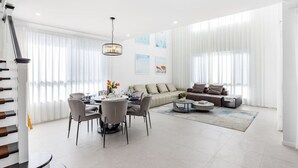 Un salon moderne comprenant un coin repas, un ensemble de canapés et un escalier.