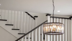 Un espace de salle à manger moderne avec une table ronde pour quatre personnes, un lustre et un escalier avec des rampes blanches.