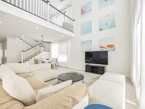 A modern living room with a sectional sofa, a flat-screen TV, and artwork on the walls. - Elegant & Convenient 4-Beds Villa w/ easy access (Upper Mount Gravatt)