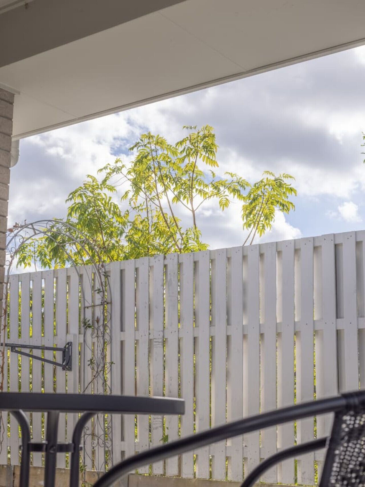 A covered patio area with a white fence, a table, and chairs.