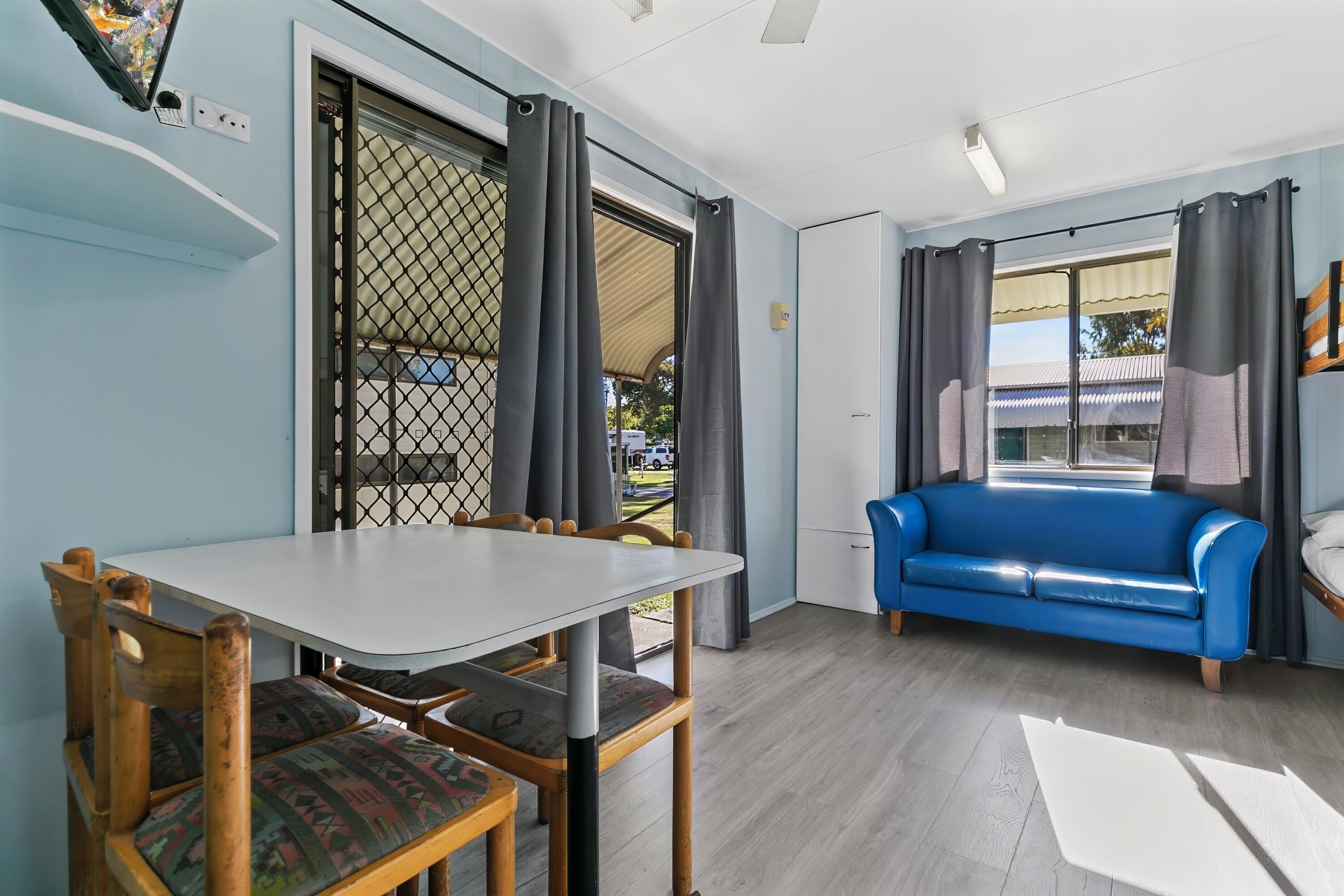 Ein Zimmer mit Esstisch, Stühlen, einem blauen Sofa und einem großen Fenster mit Vorhängen.