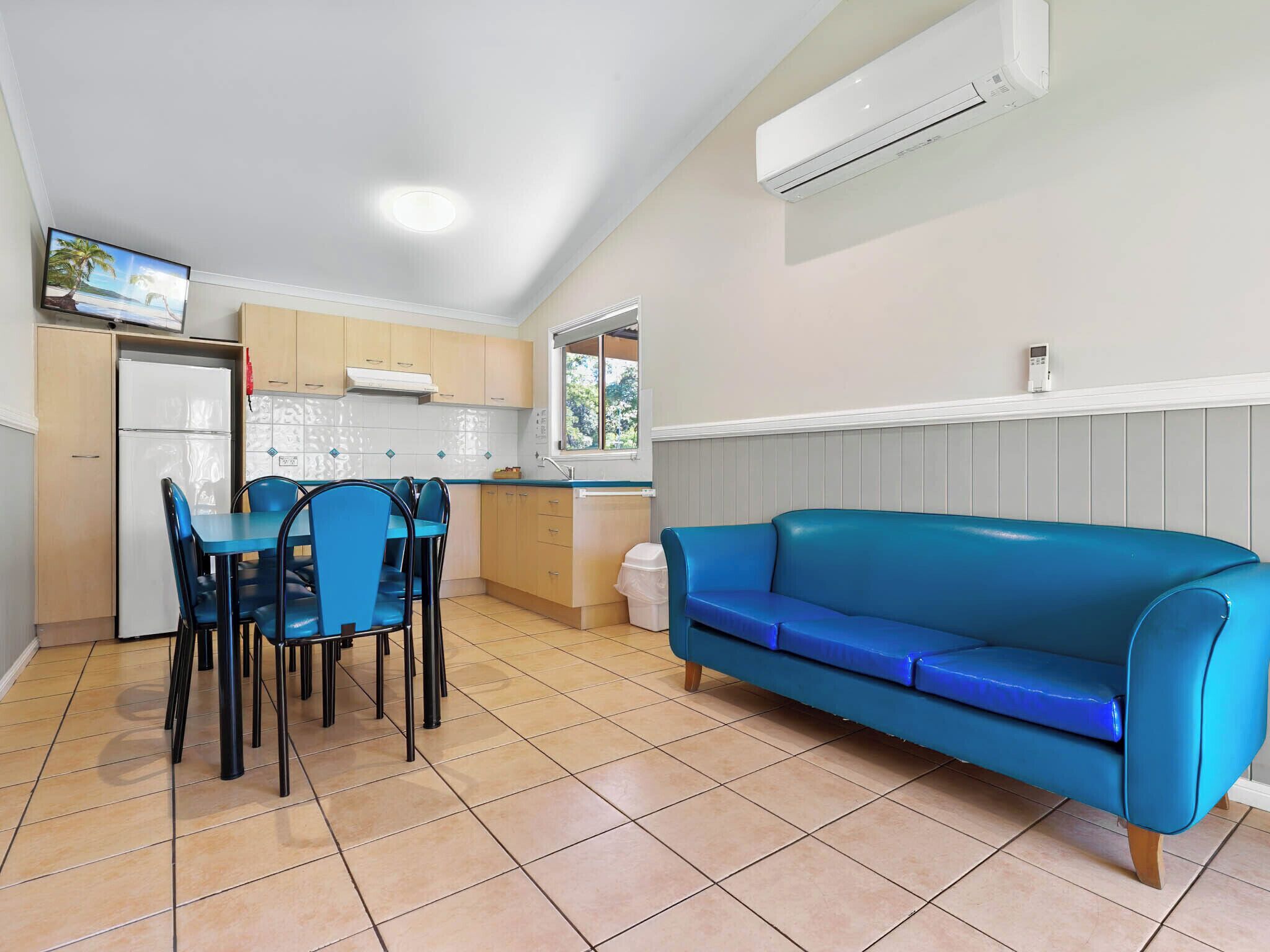 Una cocina compacta con comedor, un sofá azul y un televisor montado en la pared.