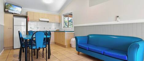 Una cocina compacta con comedor, un sofá azul y un televisor montado en la pared.